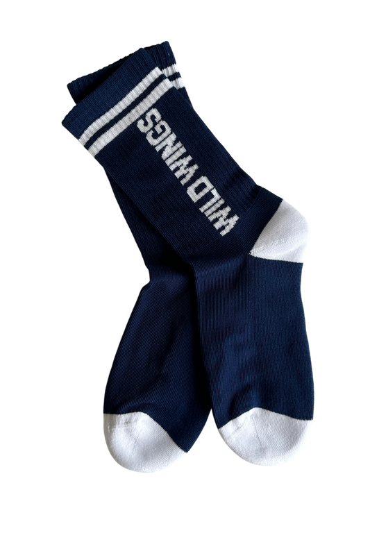 Ein Paar gerippte navyblaue Sportsocken mit weißem Zehen- und Fersenbereich. In Großbuchstaben ist auf dem Schaft von unten nach oben WILD WINGS in weiß eingestrickt. Sportliches Design mit zwei weißen dünnen Streifen am oberen Bund. Der Sohlenbereich ist Innen frottiert.